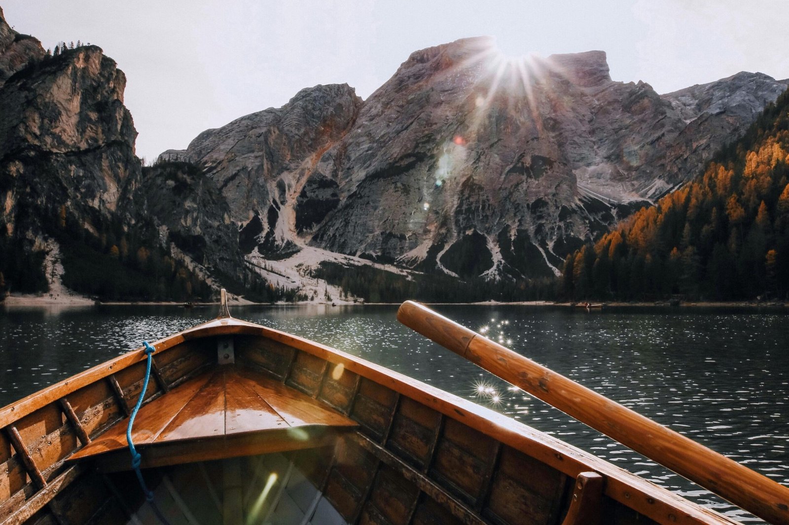 Gallery Wooden boat sailing on a serene mountain lake with sunrays illuminating the scenic landscape.