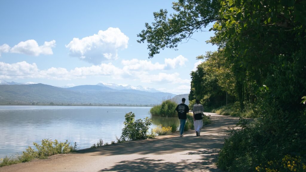 A scenic view of a couple walking along Ioannina lake in Greece under a clear blue sky.